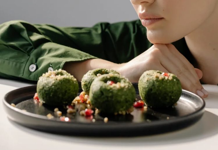 Close-up of spinach pkhali, a Georgian vegan dish, with a woman in green observing.